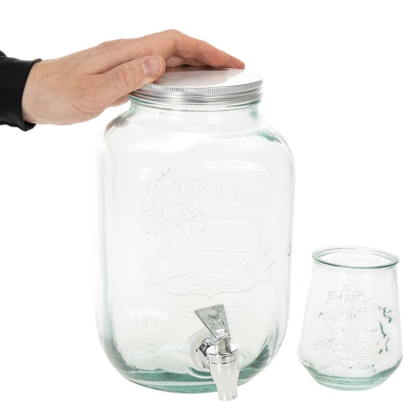 Getränkespender aus Recyclingglas mit Zapfhahn, Metalldeckel und passendem Trinkglas. Eine Hand zeigt den Größenvergleich.