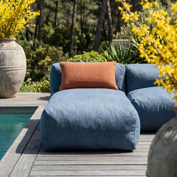 Modulares blaues Gartensofa mit orangefarbenem Dekokissen auf einer Holzterrasse am Pool.