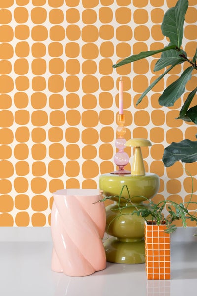 Helle Innenszene mit geometrischer Retro-Tapete mit orangefarbenen abgerundeten Quadraten, bunten Beistelltischen, Kerzenständer und Pflanzen.