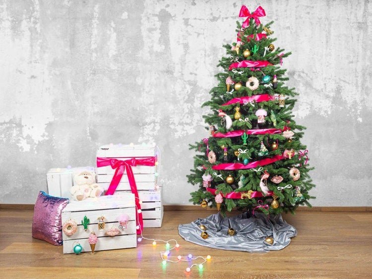 Geschmückter künstlicher Weihnachtsbaum mit pinkem Band und verspielten Anhängern, kombiniert mit weißen Holzkisten und einer Lichterkette.