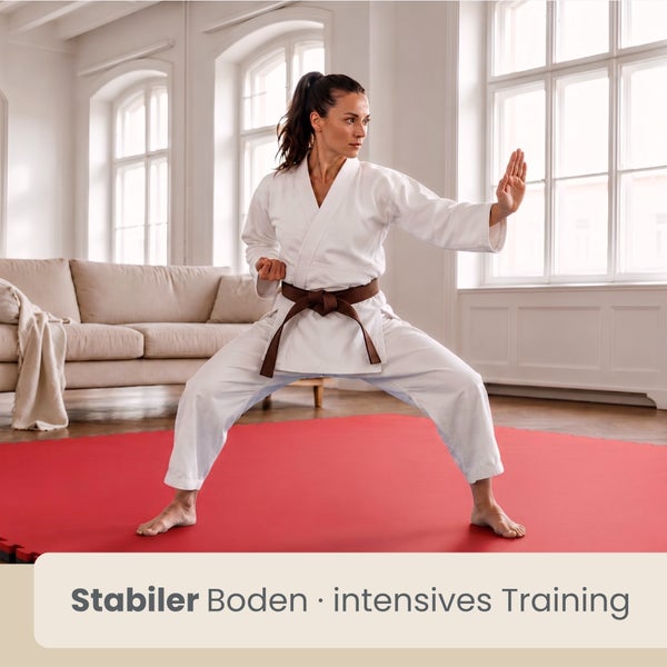 Frau im Karateanzug trainiert auf einer roten Sportmatte in einem hellen Wohnzimmer. Text: Stabiler Boden, intensives Training.
