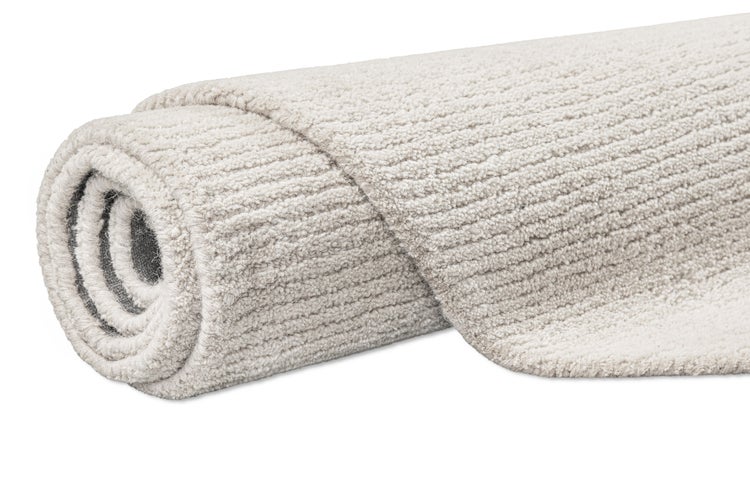 Zusammengerollter, heller Teppich mit strukturierter, gerippter Oberfläche.