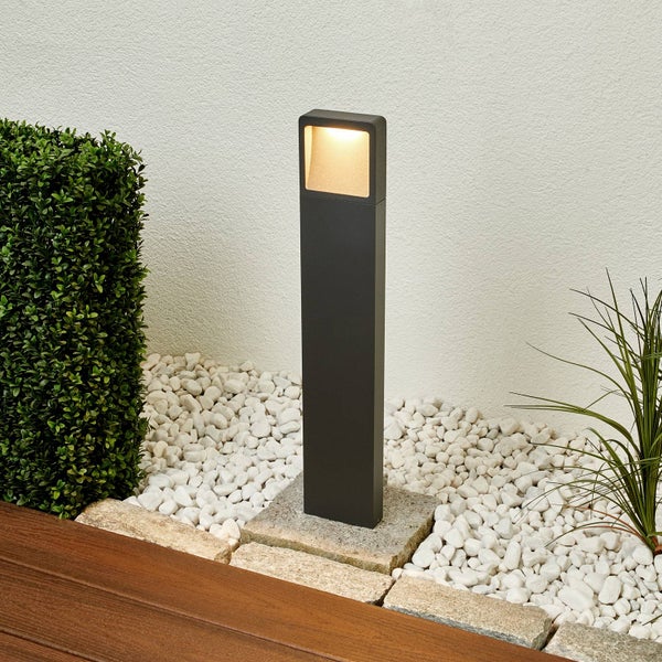 Moderne anthrazitfarbene LED Wegeleuchte in einem Gartenbeet mit weißen Ziersteinen und einer grünen Hecke.