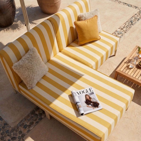 Gestreiftes Outdoor-Ecksofa in Gelb und Weiß auf einer sonnigen Terrasse mit Dekokissen und Loungetisch.