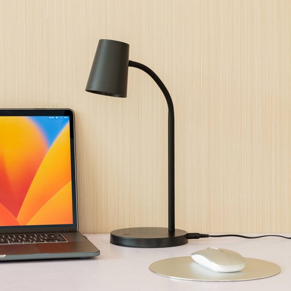 Moderne schwarze Schreibtischlampe mit flexiblem Hals an einem organisierten Arbeitsplatz mit Laptop und Maus vor einer Holzwand.