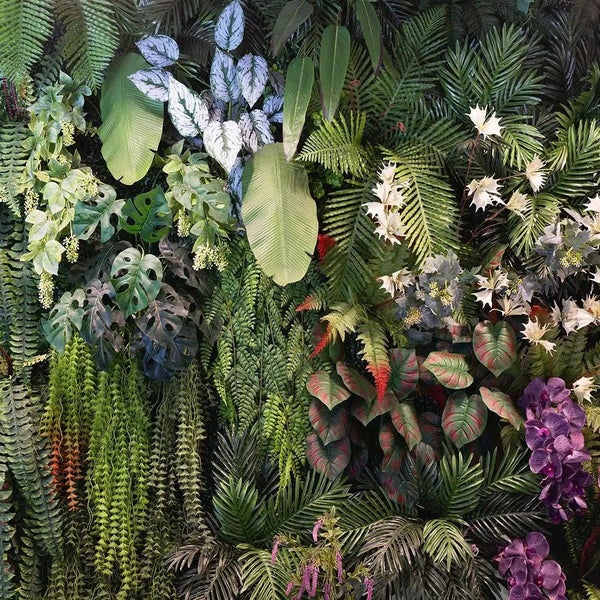 Künstliche Pflanzenwand mit tropischen Pflanzen wie Farnen, Monstera-Blättern, Palmenwedeln und Orchideen.
