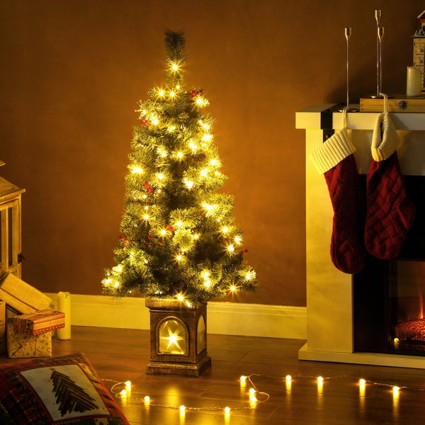 Künstlicher Weihnachtsbaum in beleuchtetem Topf mit warmweißen LED-Lichtern, festlich dekoriert neben einem Kamin mit Weihnachtsstrümpfen.