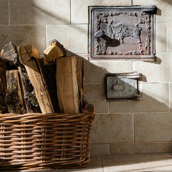 Korb mit Holz neben Ofenklappe an der Wand