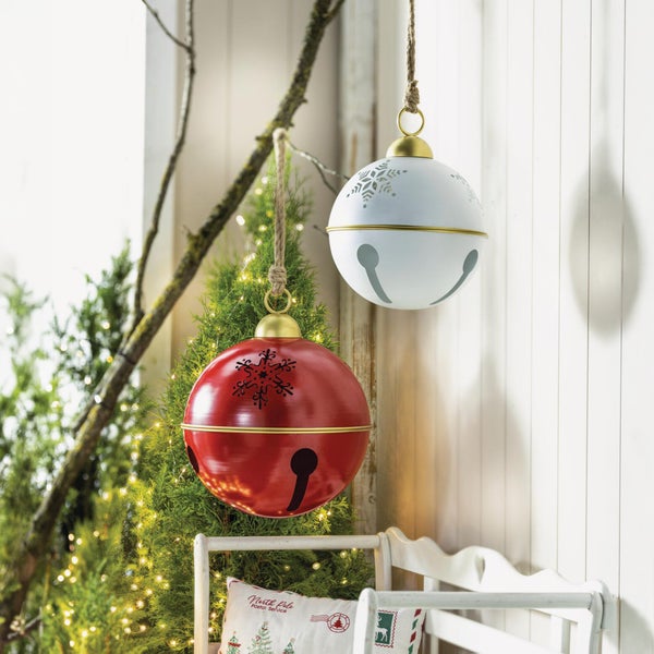 Zwei runde Metallglocken als Weihnachtsdekoration zum Aufhängen mit Schneeflockenmotiv vor einer beleuchteten Tanne.