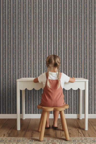 Vliestapete mit vertikalem Streifen- und Blumenmuster in einem hellen Kinderzimmer mit weißem Schreibtisch und Holzschemel.