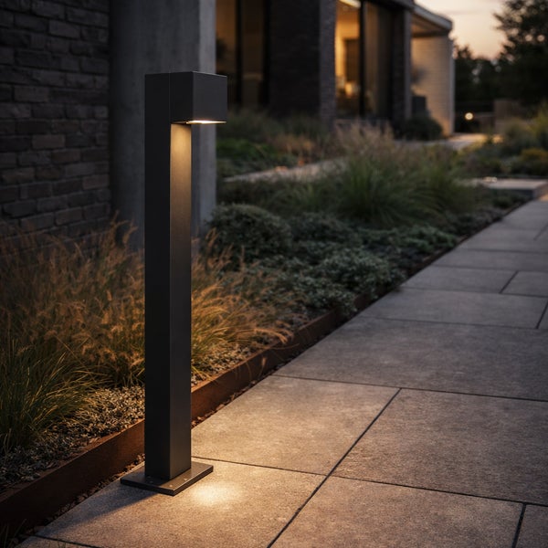 Moderne rechteckige LED-Wegeleuchte in Dunkelgrau beleuchtet einen Steinweg in einem Garten.