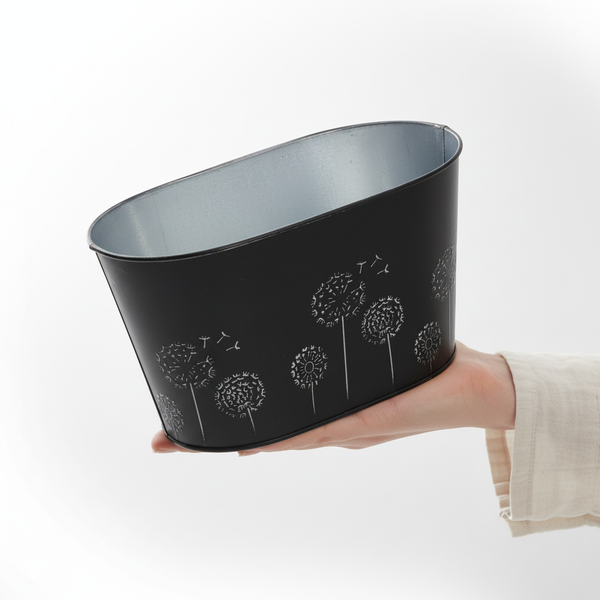 Ovaler schwarzer Zinktopf mit Pusteblumen-Motiv, in einer Hand gehalten.