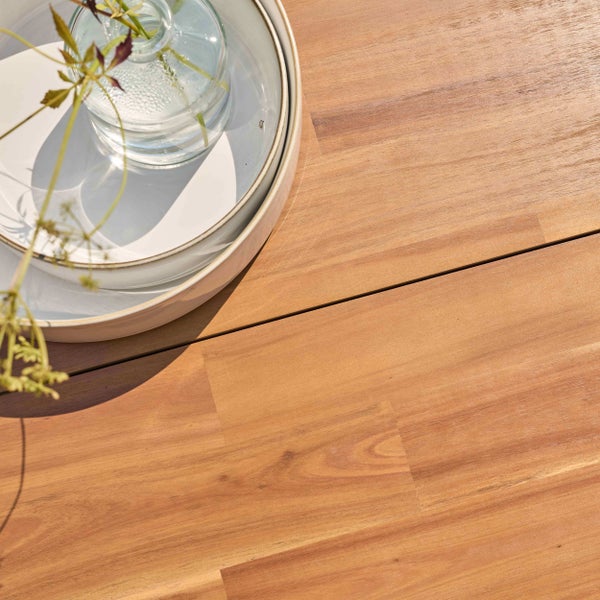 Nahaufnahme einer hölzernen Gartentischoberfläche mit Holzmaserung, darauf stehen eine Keramikschale und eine Glasvase mit einer Pflanze.