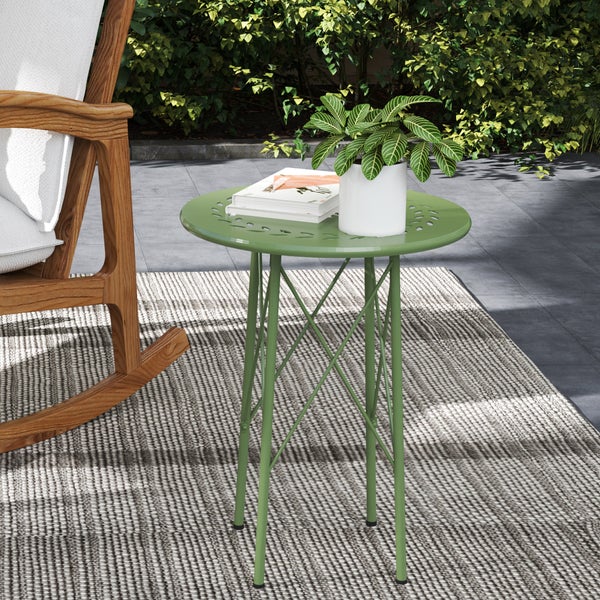 Ein runder, grüner Beistelltisch aus Metall auf einer Terrasse mit Teppich, neben einem hölzernen Schaukelstuhl.