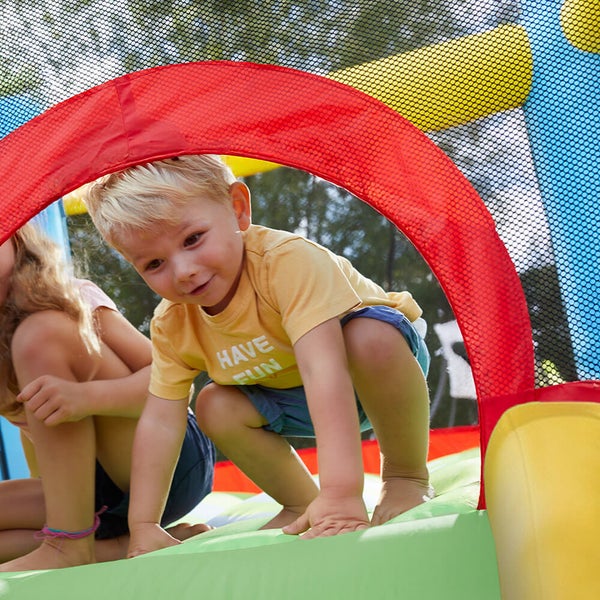 Ein Kind spielt in einer aufblasbaren Hüpfburg im Garten und kriecht durch eine Öffnung.