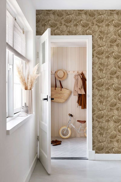 Wohnraum mit einer Wand, die mit einer Tapete mit floralem Muster in Naturtönen tapeziert ist, Blick in einen Flur mit Garderobe und Laufrad.