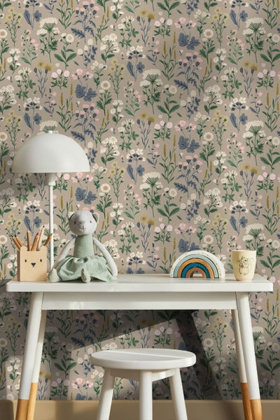 Vliestapete mit Wildblumenmuster in einem Kinderzimmer hinter einem weißen Schreibtisch mit Spielzeug und einer Tischlampe.