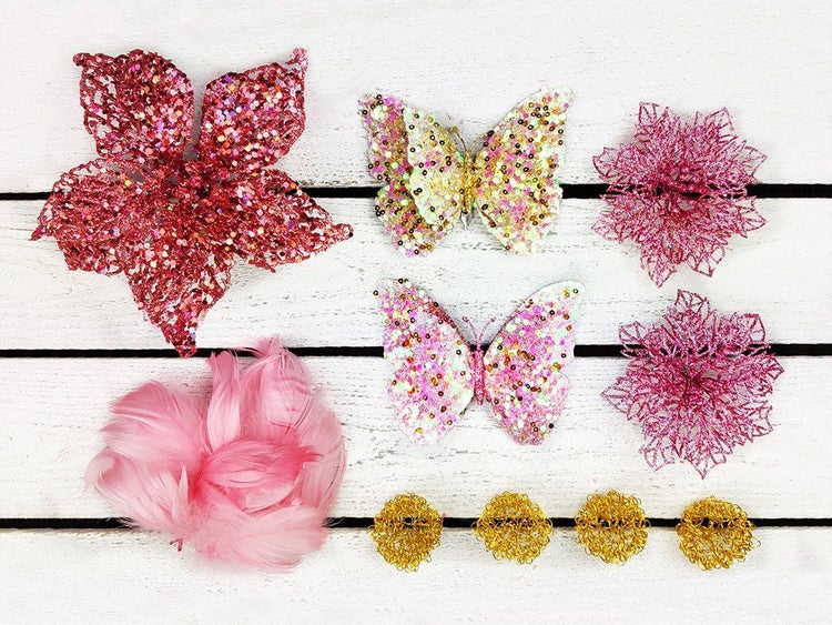 Dekorationsset mit glitzernden Kunstblumen, Schmetterlingen, einer Federblume und kleinen drahtartigen Elementen auf einer Holzoberfläche.