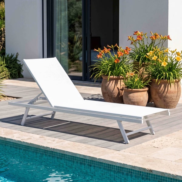 Weiße Sonnenliege auf einer Terrasse am Pool, neben Pflanzkübeln mit Blumen.