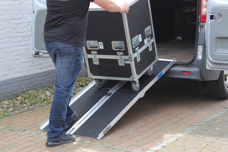 Eine Person schiebt einen Rollcontainer über eine Rampe in einen Transporter.