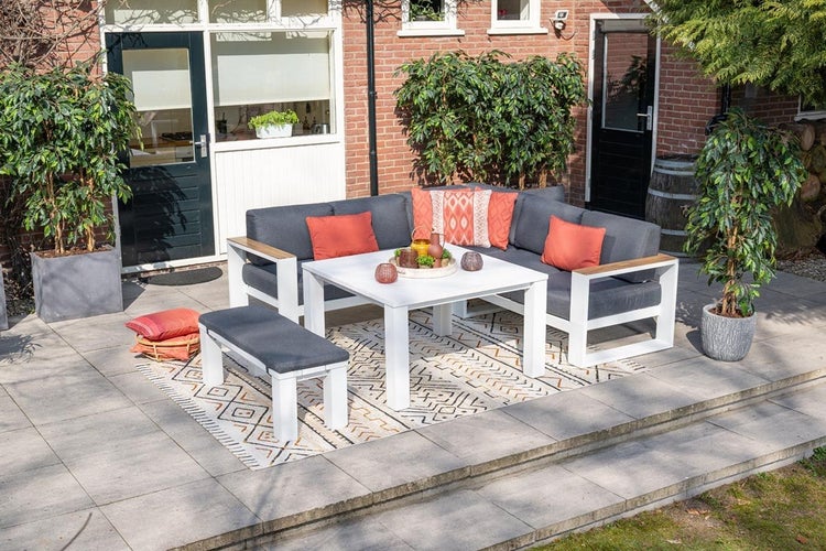 Modernes Garten-Lounge-Set aus weißem Aluminium mit Ecksofa, Sitzbank und quadratischem Tisch auf einer Terrasse.