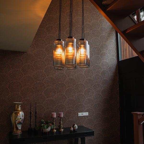 Dreiflammige Pendelleuchte mit zylindrischen Glasschirmen über einem Sideboard in einem modern eingerichteten Raum mit gemusterter Tapete.