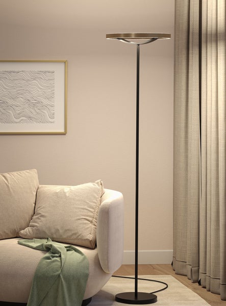 Moderne Stehleuchte mit schwarzem Standbein und Metallelementen in einem minimalistischen Wohnzimmer mit beigem Sofa und Vorhängen.