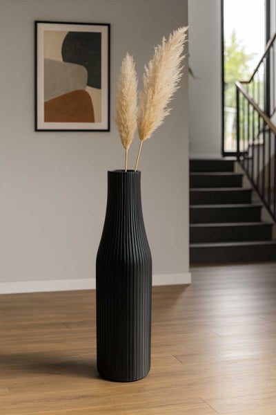 Hohe, geriffelte schwarze Bodenvase mit Pampasgras auf Holzboden in einem modernen, hellen Interieur mit Treppe und Wandbild.
