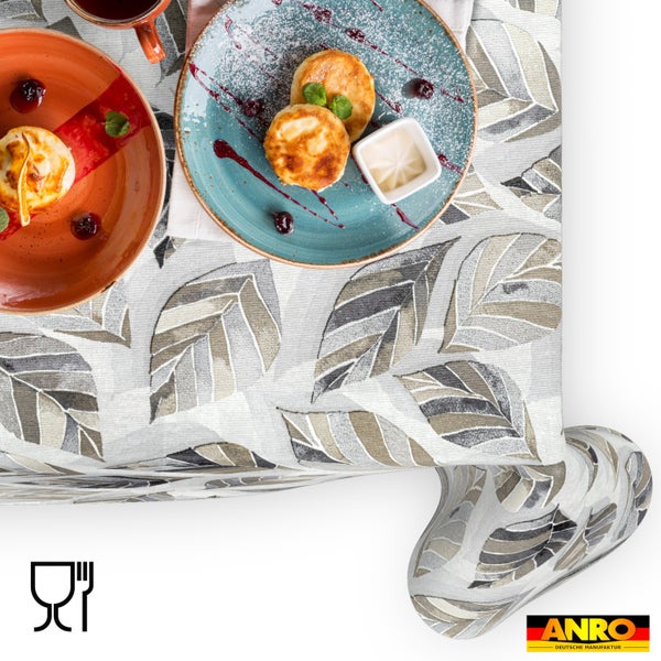 Tischdecke mit großem Blättermuster auf einem gedeckten Tisch mit Frühstückstellern. Lebensmittelecht. ANRO Logo.