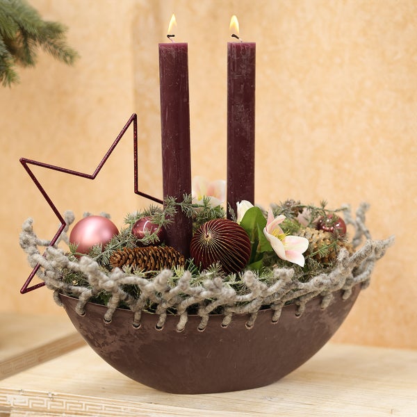 Adventsgesteck mit zwei brennenden Kerzen, Stern, Kugeln und Tannenzapfen in einer Schale.