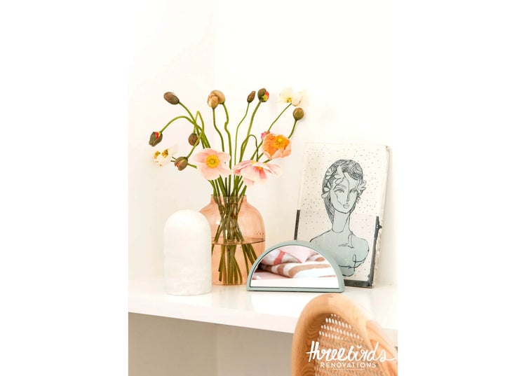 Dekorative Inneneinrichtung mit einer Glasvase voller Blumen, einem kleinen halbrunden Tischspiegel, einer Skizze und einer weißen Steinfigur.