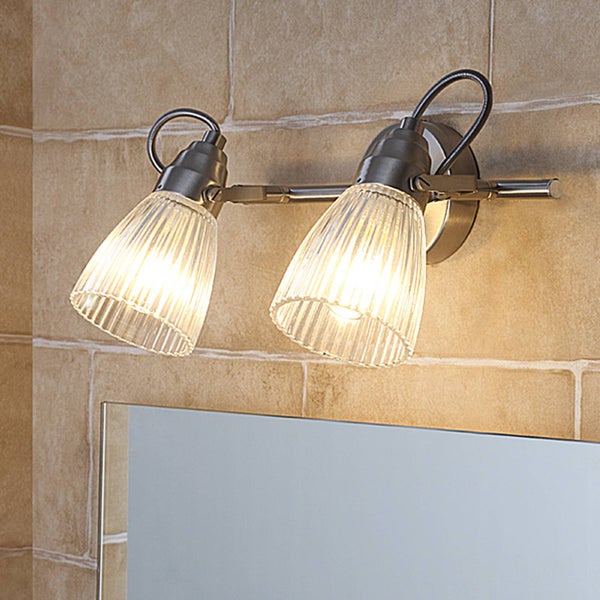 Badwandleuchte zweiflammig mit gerippten Glasschirmen und Metallgestell über einem Spiegel an einer gefliesten Wand.