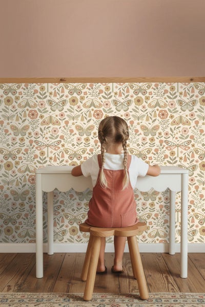 Mädchen sitzt an einem Schreibtisch vor einer Wand mit floral gemusterter Tapete