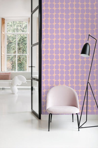 Wohnraum mit einer Tapete mit retro-geometrischem Muster aus abgerundeten Quadraten, einem hellrosa Samtsessel und einer schwarzen Stehlampe.