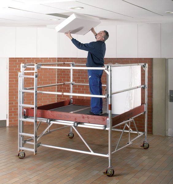 Eine Person auf einem fahrbaren Gerüst montiert eine Deckenplatte.