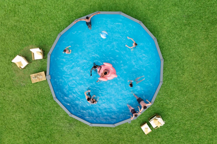 Luftaufnahme eines runden Aufstellpools mit grauem Rahmen auf Rasen, in dem Personen schwimmen und ein aufblasbarer Flamingo treibt.