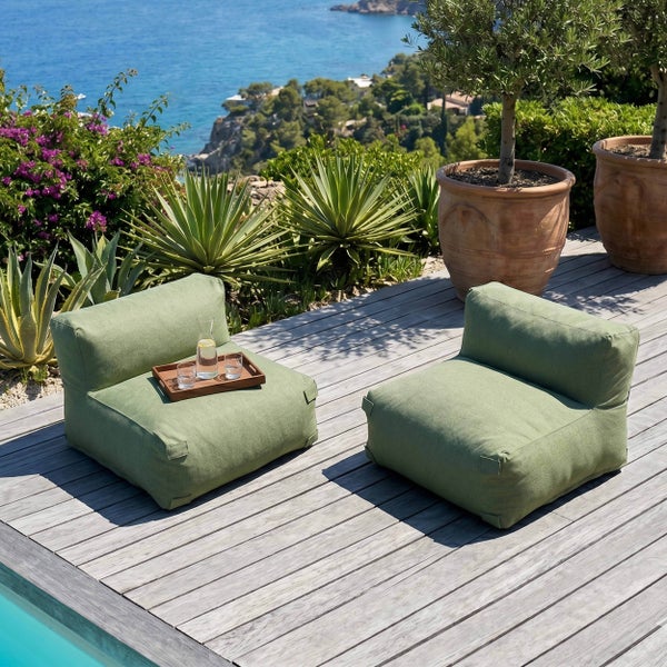 Zwei grüne Outdoor Loungesessel auf einer Holzterrasse mit Meerblick und mediterraner Bepflanzung.