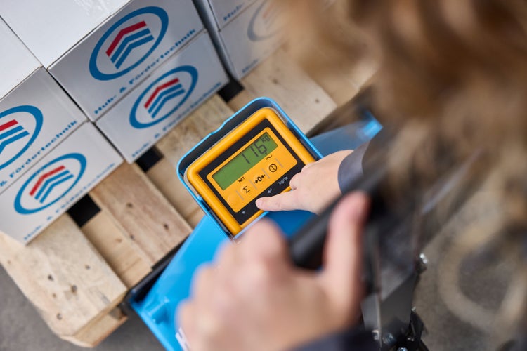 Nahaufnahme der Digitalanzeige eines Hubwagens mit Waage, die 116 Kilogramm anzeigt, während eine Person eine Taste bedient.