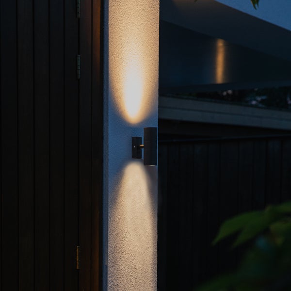 Moderne Außenwandleuchte mit Lichtaustritt nach oben und unten an einer strukturierten Hauswand.