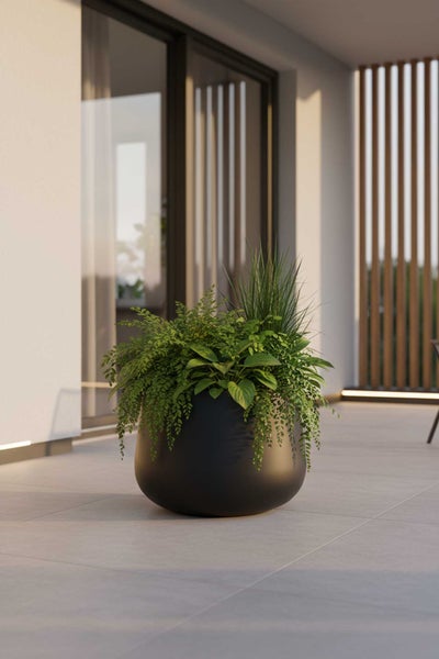 Runder schwarzer Pflanzkübel mit verschiedenen grünen Pflanzen auf einer modern gestalteten Terrasse mit hellen Bodenfliesen.