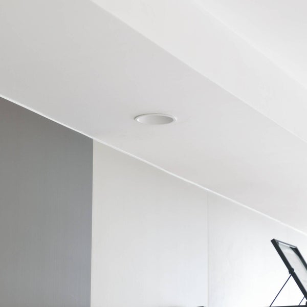 Runder weißer Einbaustrahler in einer hellen Decke über einer modernen Wandgestaltung in Grau und Weiß.