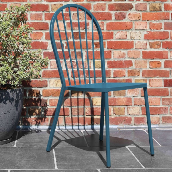 Blauer Metall-Gartenstuhl mit hoher Sprossen-Rückenlehne und konischen Beinen auf einer Steinterrasse vor einer Ziegelwand.