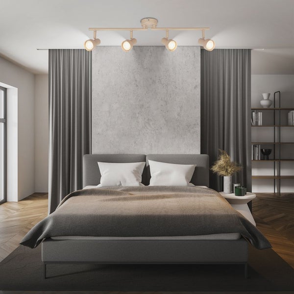 Moderne Deckenleuchte mit vier verstellbaren Strahlern in einem hellen Schlafzimmer mit grauem Bett und Wand in Betonoptik.