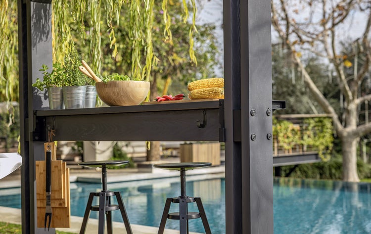Szene einer Outdoor-Küche mit Hochstühlen, auf der sich eine Schüssel mit Salat, Maiskolben und Kräutertöpfe befinden