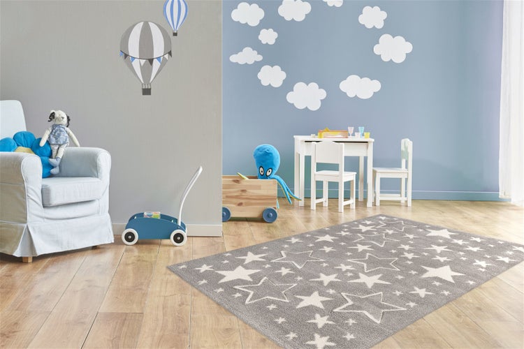 Ein Kinderzimmer mit einem Teppich mit Sternenmuster, einem Kindertisch und Stühlen, Spielzeugkiste und Spielzeugwagen auf Holzboden.