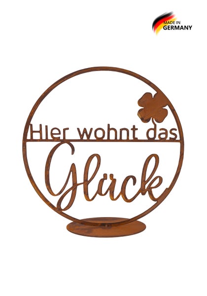 Runder Aufsteller aus Metall in Edelrost-Optik mit dem Schriftzug Hier wohnt das Glück und einem Kleeblatt.