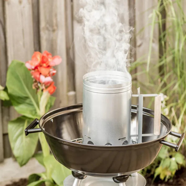 Anzündkamin aus Metall mit Holzgriff auf einem runden Holzkohlegrill im Garten.