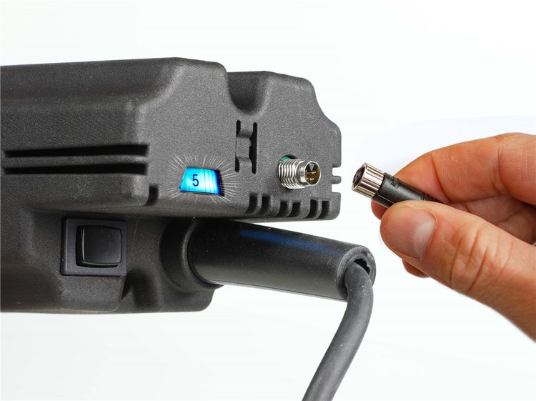 Eine Hand verbindet ein Kabel mit dem Anschluss eines technischen Geräts mit digitaler Anzeige.