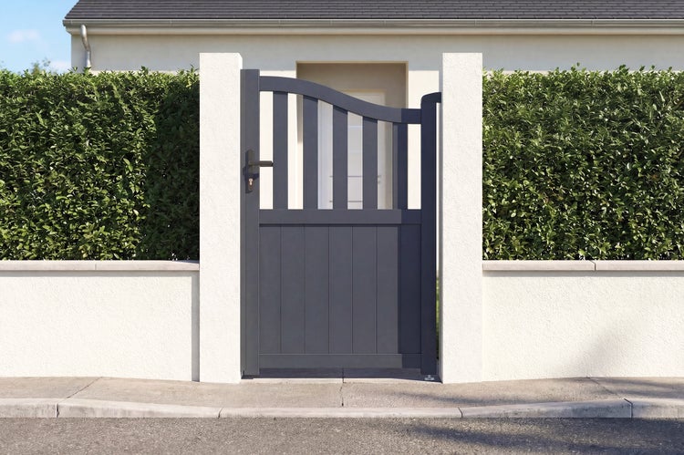 Anthrazitfarbenes Aluminium-Gartentor mit geschwungenem Oberteil und vertikalen Stäben zwischen zwei weißen Pfeilern vor einer Hecke.