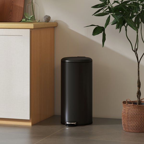 Schwarzer Tretmülleimer aus Metall in einer hellen, modern eingerichteten Küche neben einem Holzunterschrank und einer Zimmerpflanze.